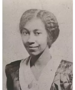 Portrait of a young Black woman with her hair parted down the middle and pulled back. She is wearing a black and white dress and is looking at the camera with a closed-mouth smile.