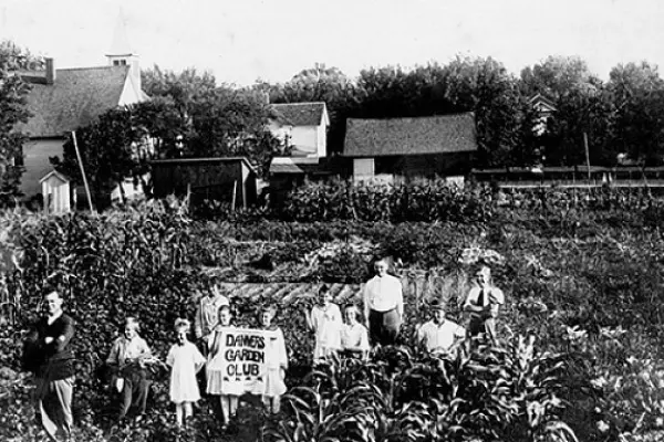Black and white photo of children in a farm field, holding a fabric sign that says Danvers Garden Club