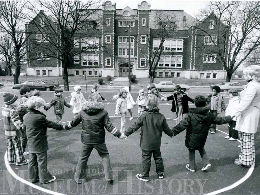 Group of children hold hands in a circle at Emerson School, 1976