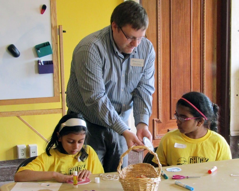 Image of one of our education staff Anthony Bowman helping two students with an educational craft